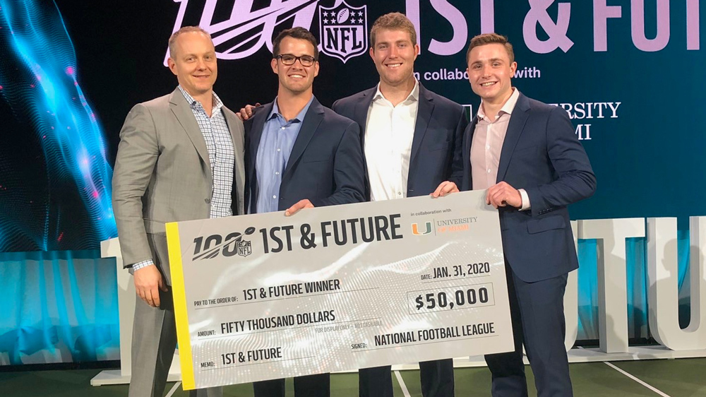 Four men stand with a giant check in front of the NFL 1st and Future logo